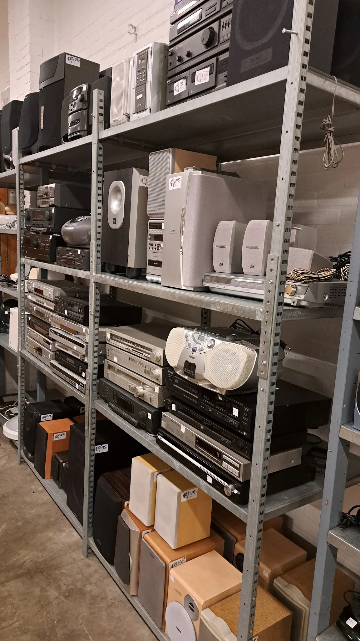 Metalen stellingkast met elektronische apparaten en speakers in tweedehands winkel