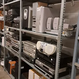 Metalen stellingkast met elektronische apparaten en speakers in tweedehands winkel