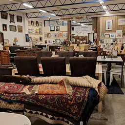 Winkelvloer met bruine stoelen, uitgestalde meubels, kunst aan muren en diverse spullen op rekken