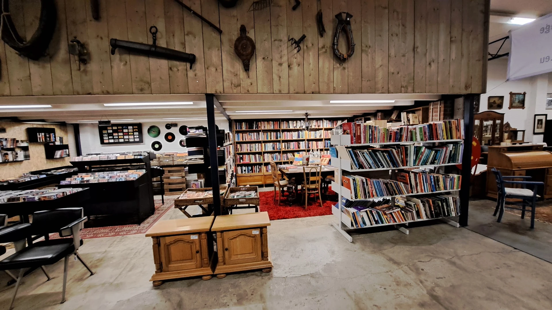 Ruim interieur van kringloopwinkel met boekenkasten, houten meubels, pianotoetsen aan muur en rode vloerkleed