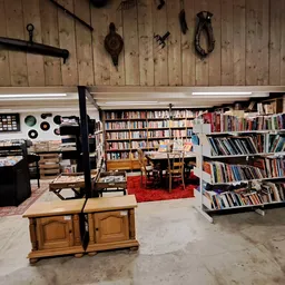 Ruim interieur van kringloopwinkel met boekenkasten, houten meubels, pianotoetsen aan muur en rode vloerkleed