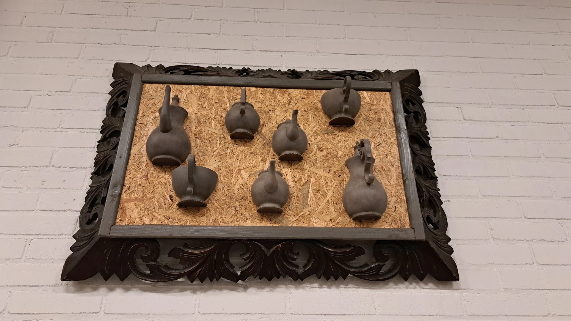 Zeven bruine keramische vazen op een kurk ondergrond in een ornamentaal zwart houten frame
