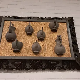 Zeven bruine keramische vazen op een kurk ondergrond in een ornamentaal zwart houten frame