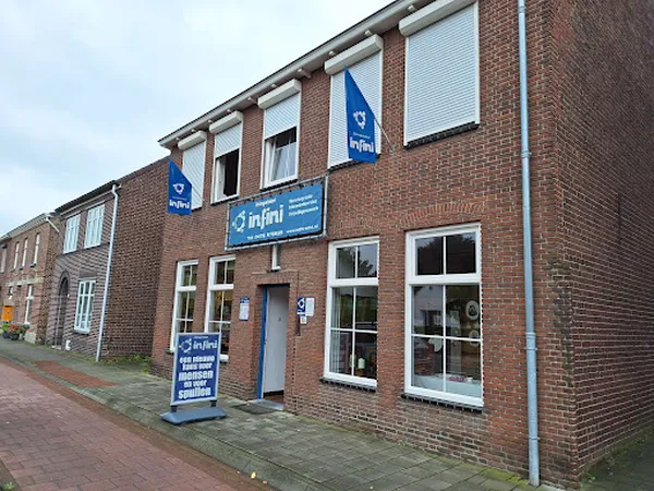 Bakstenen gevel van kringloopwinkel Kringwinkel Infini met blauwe uithangborden en entree