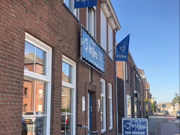Voorgevel van kringloopwinkel met bakstenen muur, witte ramen en blauwe uithangborden met logo