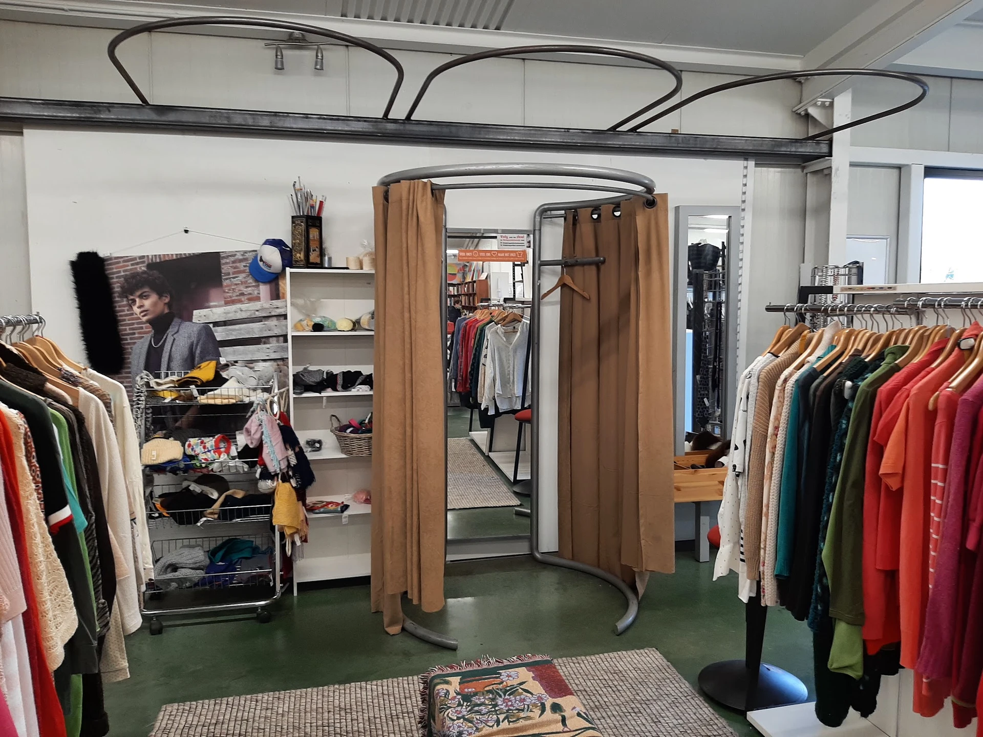 Winkelinterieur met kledingrekken vol tweedehands kleding, paskamers met bruine gordijnen en diverse winkelinrichtingen