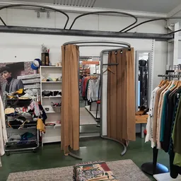 Winkelinterieur met kledingrekken vol tweedehands kleding, paskamers met bruine gordijnen en diverse winkelinrichtingen