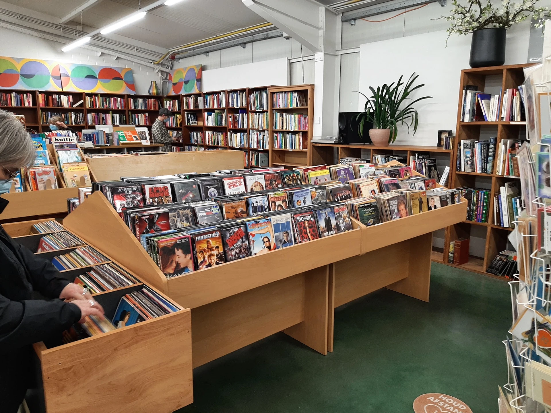 Houten uitstallingskasten met cd's, dvd's en ander media in een kringloopwinkel met boekenkasten op de achtergrond