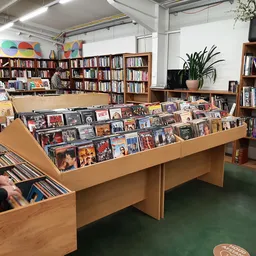 Houten uitstallingskasten met cd's, dvd's en ander media in een kringloopwinkel met boekenkasten op de achtergrond