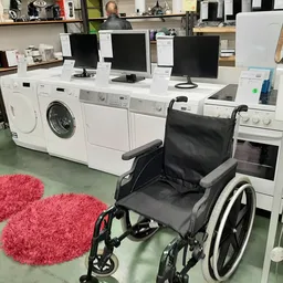 Winkelinterieur met witgoedapparaten, computermonitoren en een rolstoel op groene vloer
