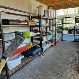 Stellingen met opgeslagen spullen in een kringloopwinkel, onder meer kusses, dozen en huishoudartikelen