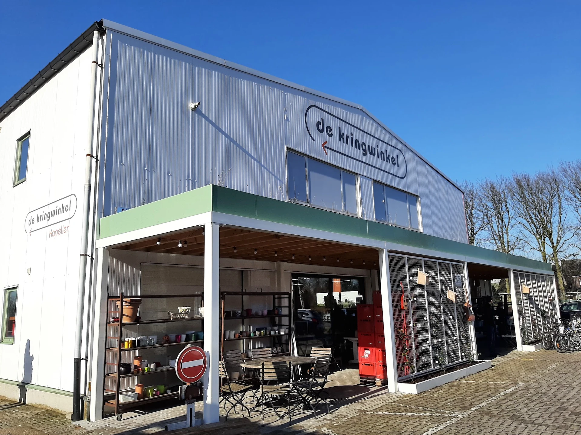 Voorgevel van kringloopwinkel met groene luifel en uitgestalde spullen in de etalage