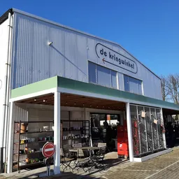 Voorgevel van kringloopwinkel met groene luifel en uitgestalde spullen in de etalage