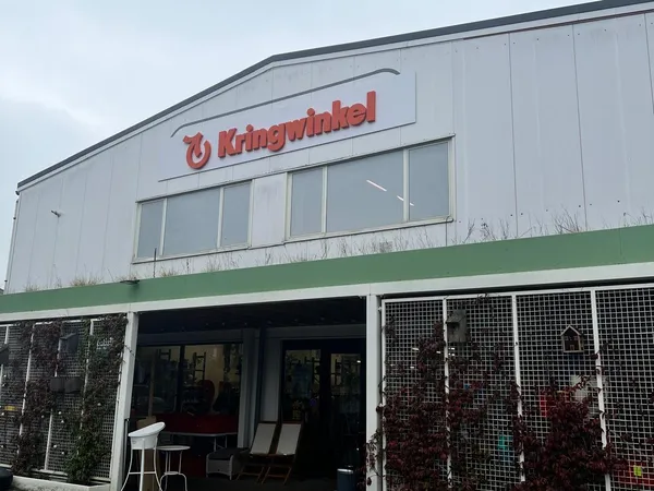 Witte gevel met groen accent van een kringloopwinkel met grote ramen en ingang
