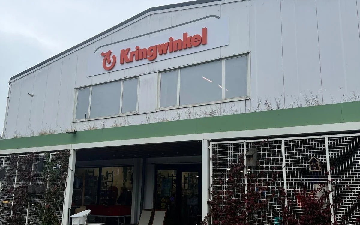 Witte gevel met groen accent van een kringloopwinkel met grote ramen en ingang