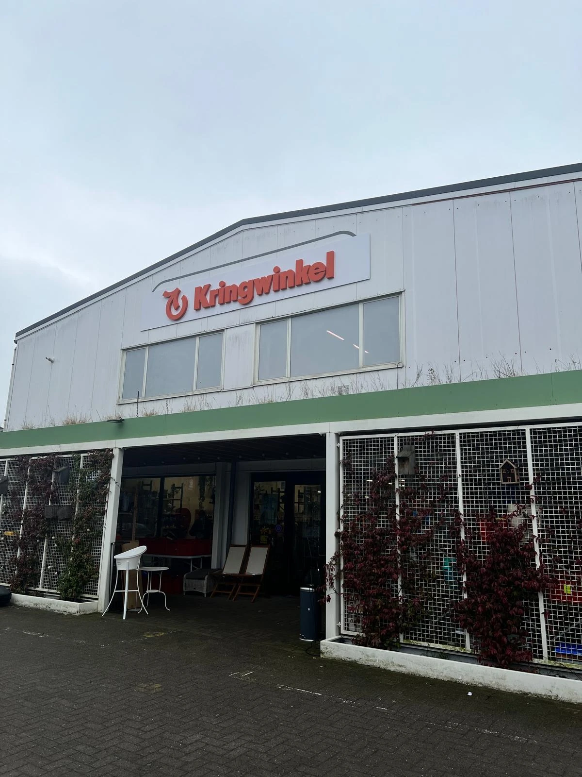 Witte gevel met groen accent van een kringloopwinkel met grote ramen en ingang