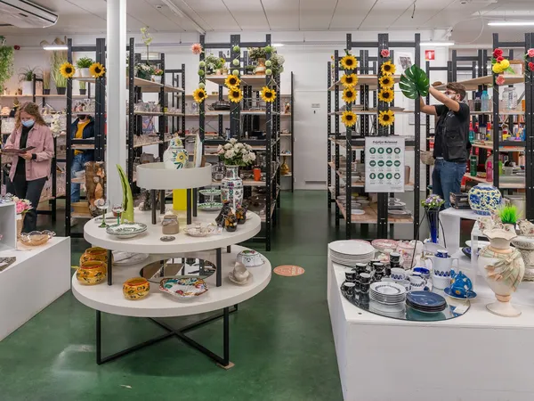 Winkelbinnenruimte met witte ronde tafels, zwarte stellingen versierd met gele zonnebloemen, uitgestalde huishoudartikelen en
