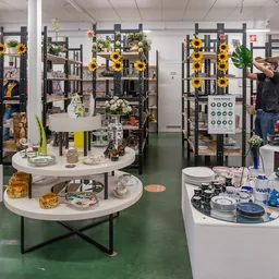 Winkelbinnenruimte met witte ronde tafels, zwarte stellingen versierd met gele zonnebloemen, uitgestalde huishoudartikelen en