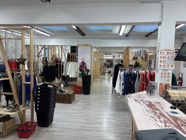 Ruim winkelinterieur met kledingrekken, houten stellingen en diversen tweedehandsartikelen verspreid over de vloer
