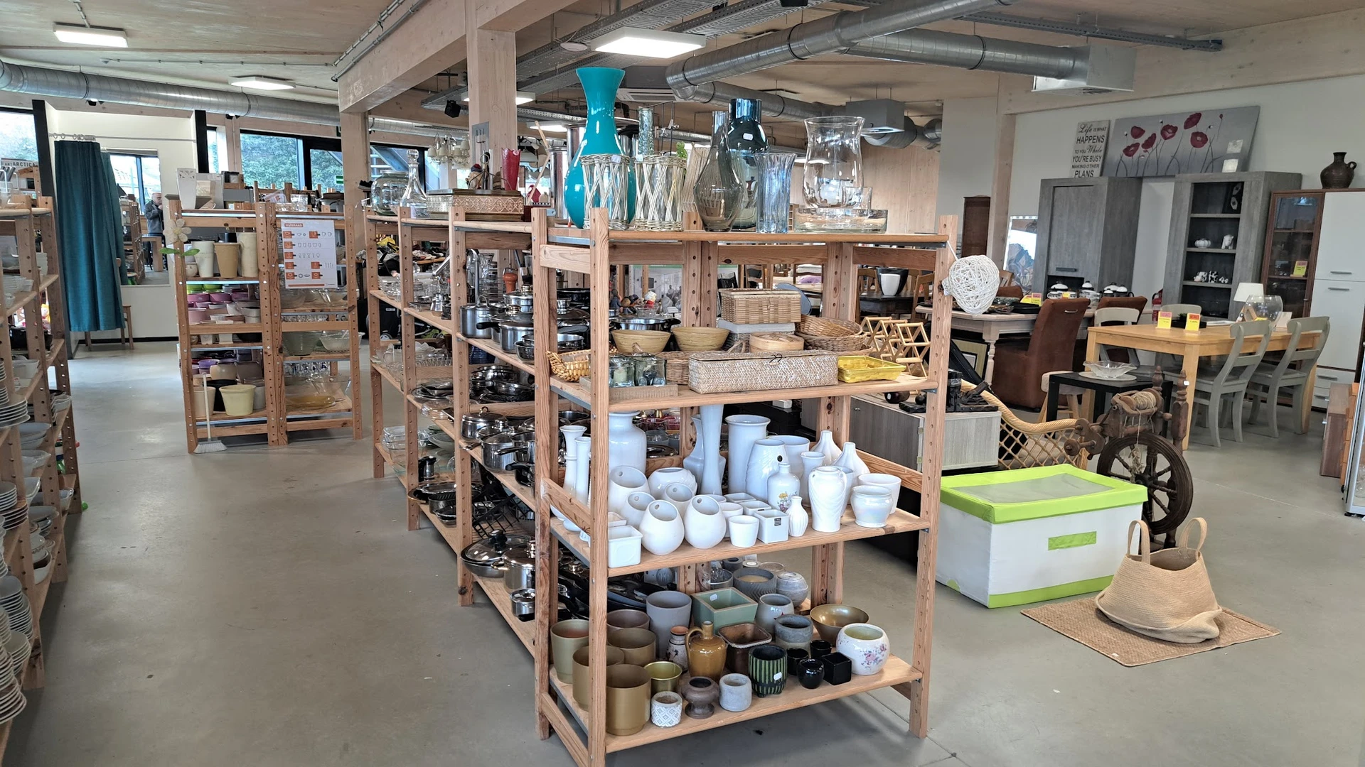 Houten stellingen met tweedehands huishoudelijke items, servies, vazen en decoratieve voorwerpen in verschillende kleuren