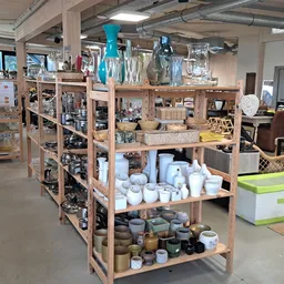 Houten stellingen met tweedehands huishoudelijke items, servies, vazen en decoratieve voorwerpen in verschillende kleuren