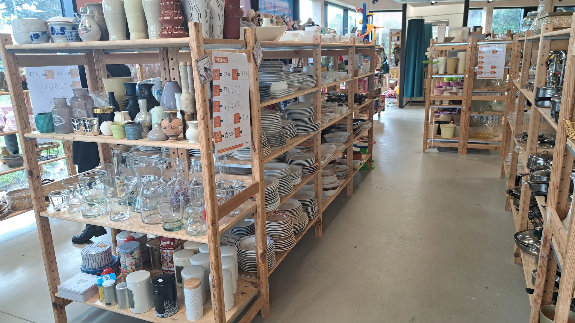 Houten stellingen gevuld met serviesgoed, borden en kopjes in een kringloopwinkel