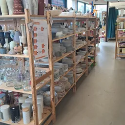 Houten stellingen gevuld met serviesgoed, borden en kopjes in een kringloopwinkel