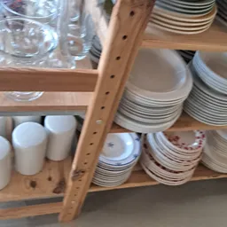 Houten stellingen met serviesgoed: gestapelde borden, kopjes en glazen