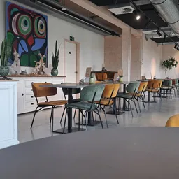 Ruime winkelruimte met houten stoelen aan tafels, kleurrijke kunstwerken aan de muur en planten als decoratie