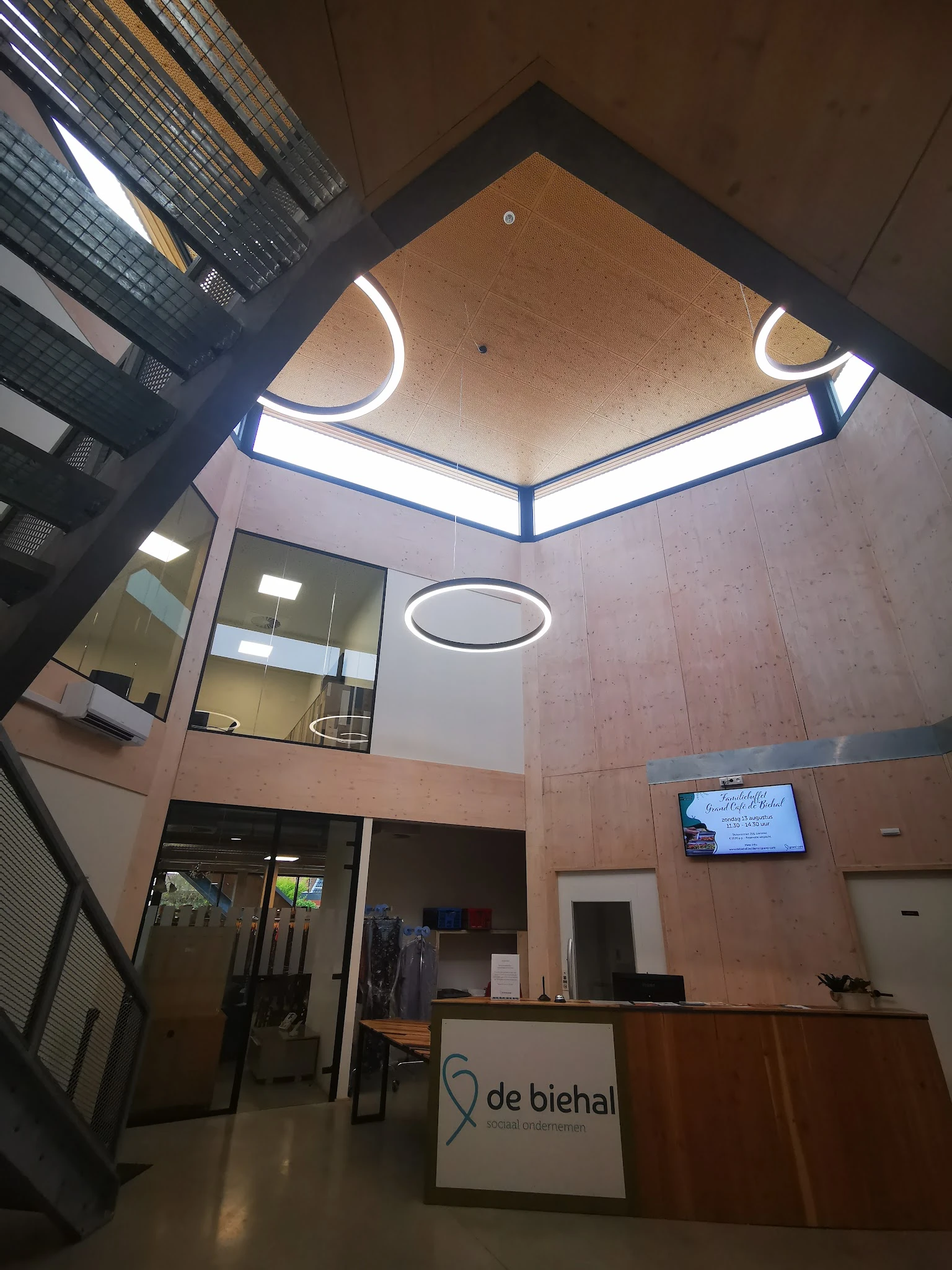 Interieur van kringloopwinkel met twee verdiepingen, glazen wand, neonverlichting aan plafond en displayscherm aan muur