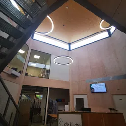 Interieur van kringloopwinkel met twee verdiepingen, glazen wand, neonverlichting aan plafond en displayscherm aan muur