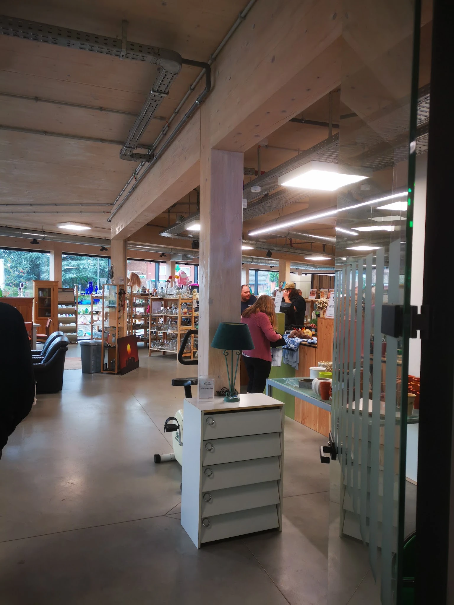 Winkelvloer van kringloopwinkel met stellingen, kasten, klanten en overheadverlichting