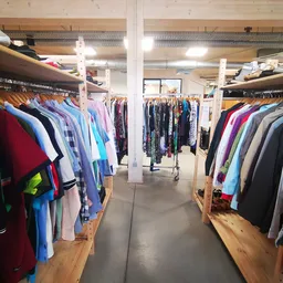 Winkelinterieur met rekken vol tweedehands kleding in verschillende kleuren, witte pilaren en betonnen vloer