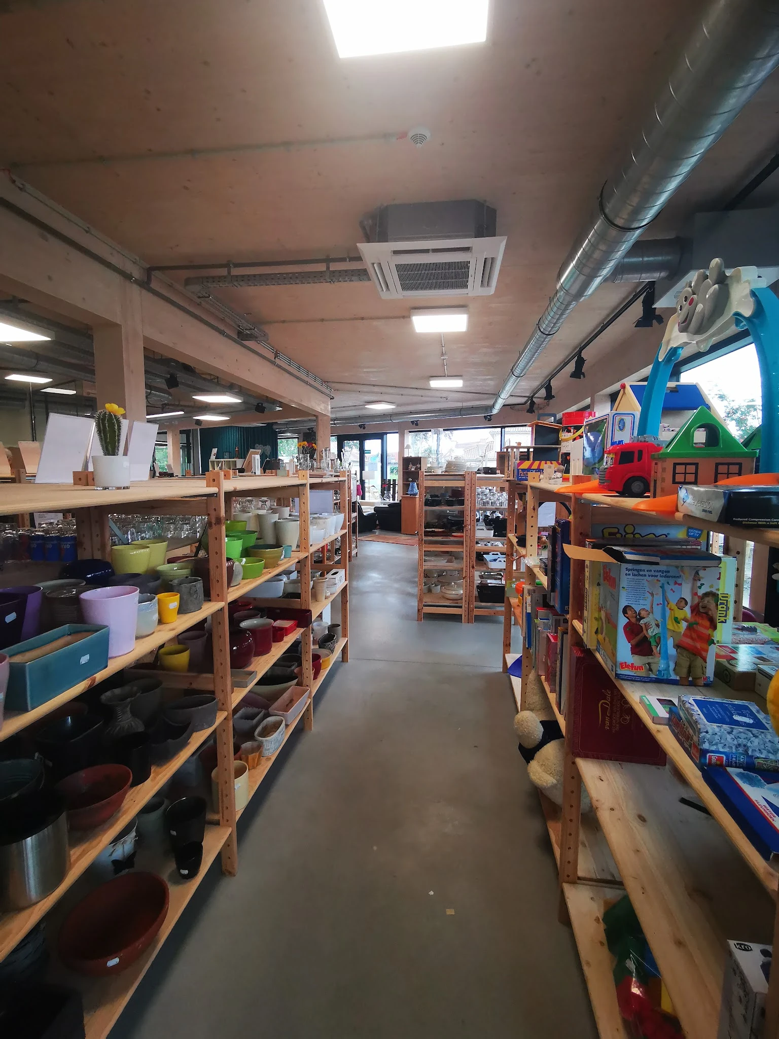 Binnenzicht van kringloopwinkel met houten stellingen vol huishoudspullen, speelgoed en gebruiksartikelen