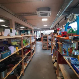 Binnenzicht van kringloopwinkel met houten stellingen vol huishoudspullen, speelgoed en gebruiksartikelen