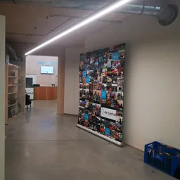 Winkelinterieur met betonnen vloer, witte wanden, lineaire plafondverlichting en een grote collage van foto's aan de muur