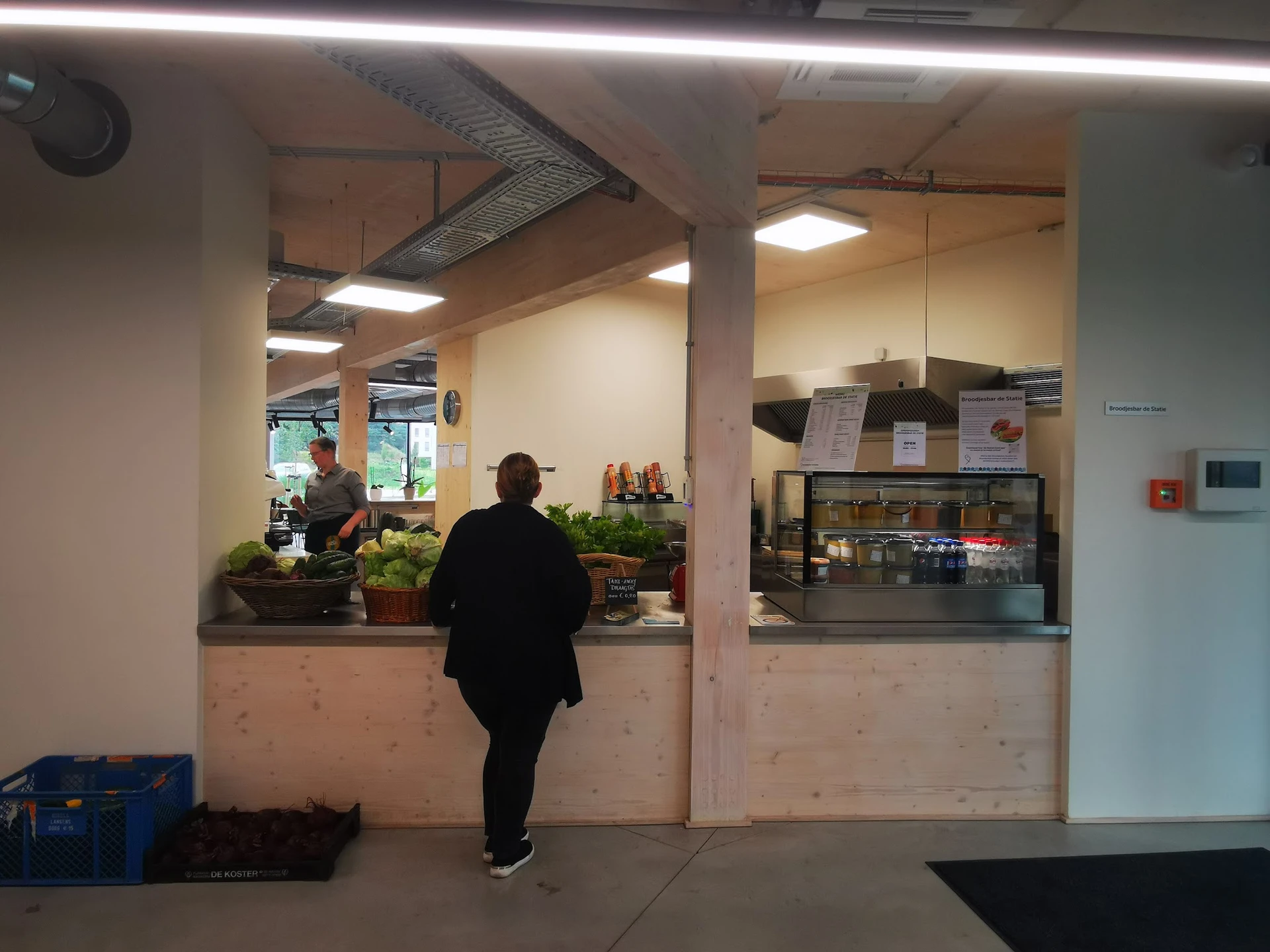 Binnenaanzicht van kringloopwinkel met toonbank, bezoeker, en verlichte winkelruimte met stellingen