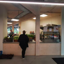 Binnenaanzicht van kringloopwinkel met toonbank, bezoeker, en verlichte winkelruimte met stellingen