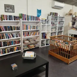 Winkelinterieur met boekenrekken langs de muur, zwarte tafel met items, en houten babybed op grijze vloer