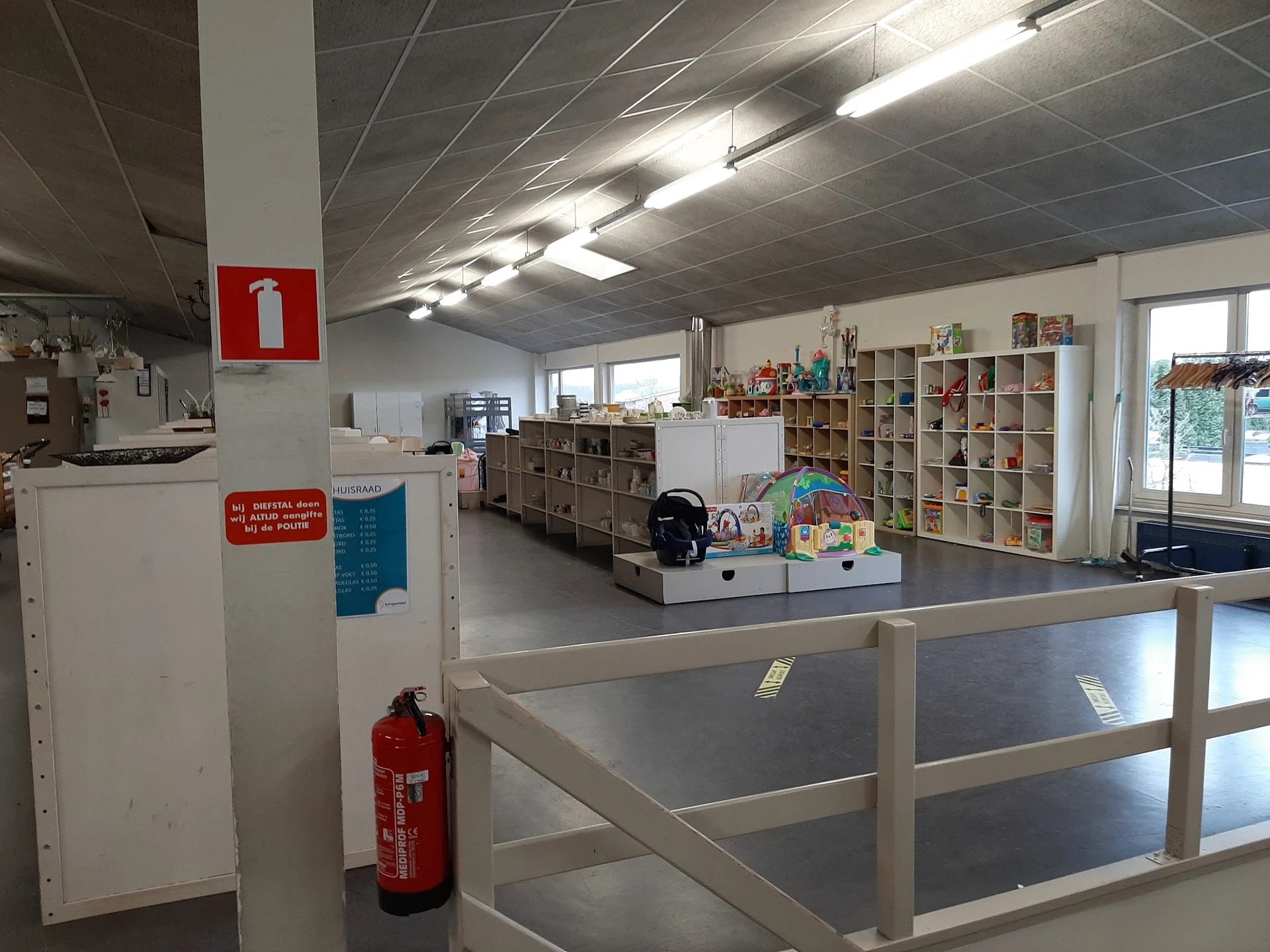 Winkelvloer met stellingen vol spullen, glazen afdeling en rood brandblusapparaat
