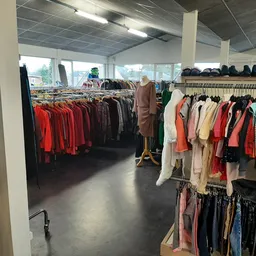 Winkelinterieur met rekken vol tweedehands kleding in verschillende kleuren en stijlen