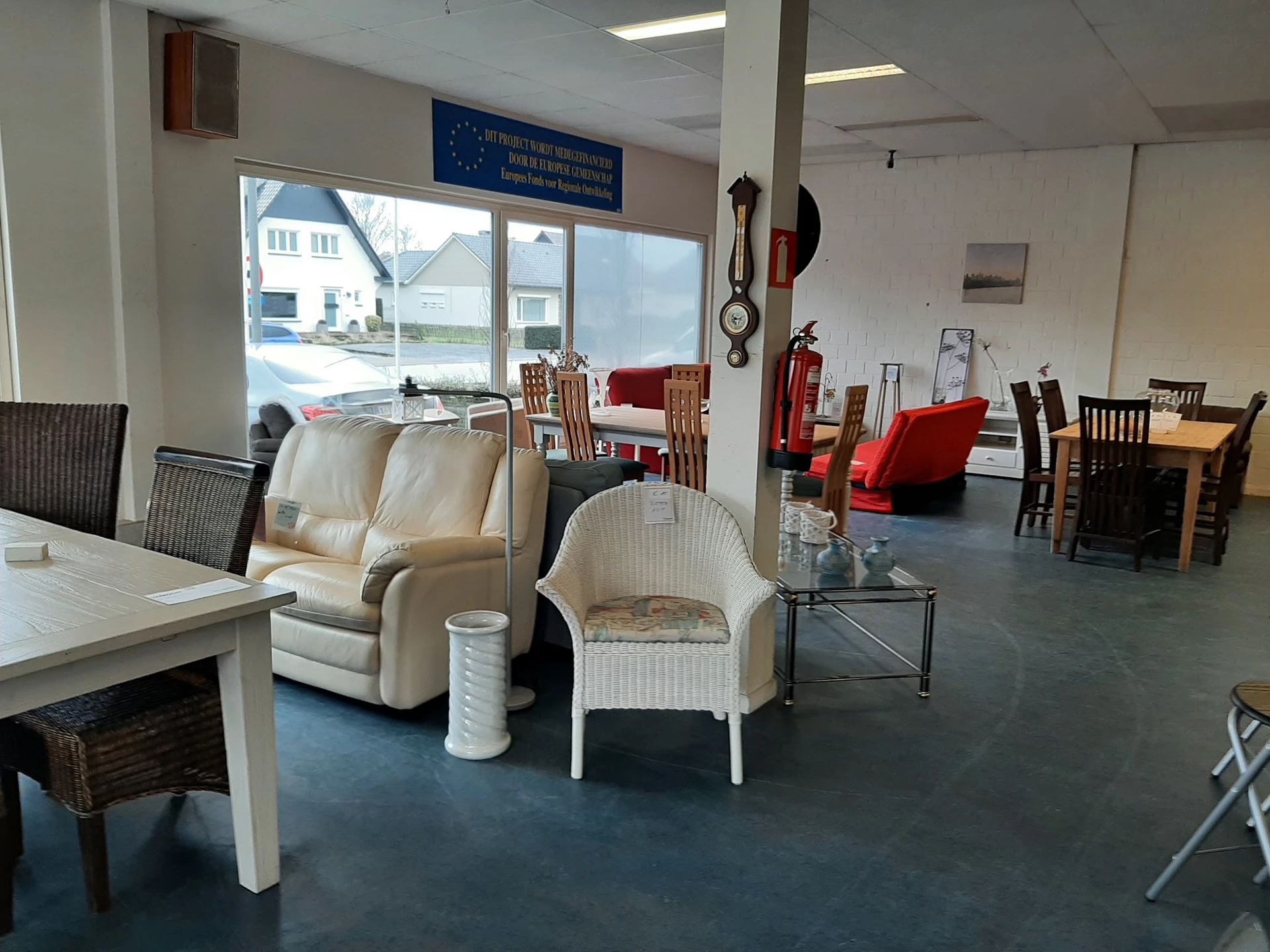 Winkelvloer met tweedehandsmeubels: fauteuils, stoelen, tafels en diverse huishoudartikelen uitgestald onder fluorescente ver