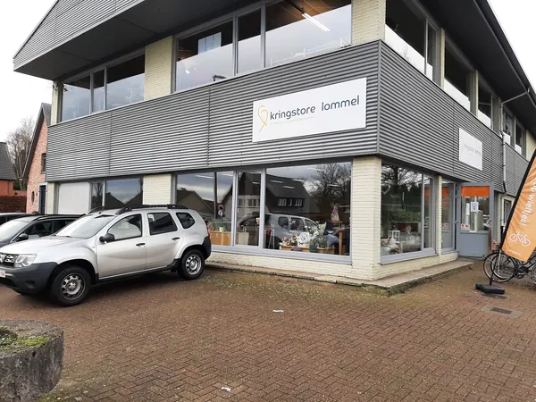 Moderne gevel van kringloopwinkel met witte auto geparkeerd ervoor en etalageramen