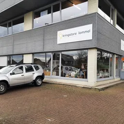Moderne gevel van kringloopwinkel met witte auto geparkeerd ervoor en etalageramen