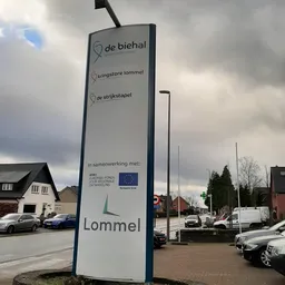 Blauw informatiebord met winkelnaam Lommel en drie aanduidingen voor verschillende afdelingen, staande voor de winkelgevel.