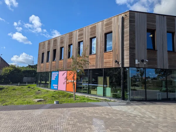 Moderne kringloopwinkel met houten en donkere gevel, grote ramen op begane grond, stellingen met spullen zichtbaar, straatvoo