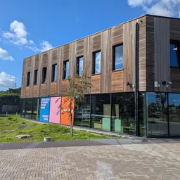 Moderne kringloopwinkel met houten en donkere gevel, grote ramen op begane grond, stellingen met spullen zichtbaar, straatvoo
