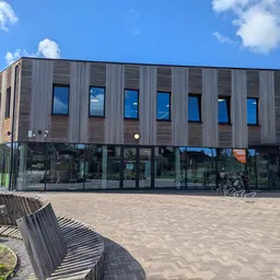 Moderne gevel van kringloopwinkel met donkergroene houten bekleding, grote ramen op begane grond en eerste verdieping, vlakke