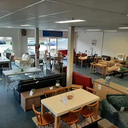 Ruim interieur van kringloopwinkel met uitgestalde meubels, tafels, stoelen en huishoudartikelen op blauwe vloer