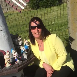 Vrouw in gele jas met zonnebril poseren naast verzameling beeldjes buiten